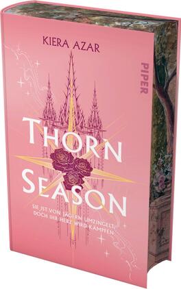 Das Buchcover zeigt einen sanften rosafarbenen Hintergrund. Zentral platziert ist der Titel „THORN SEASON“ in großen, weißen Buchstaben, umgeben von zarten, stilisierten Rosen in tiefem Rot. Über dem Titel erstrecken sich strahlende goldene Linien und Symbole, die Spannung und Magie vermitteln. Am oberen Rand befindet sich der Name der Autorin, Kiera Azar, in eleganter Schrift. Unter dem Titel steht der Satz „Sie ist von Jägern umzingelt, doch ihr Herz wird kämpfen“ in klarer, schmaler Schrift.