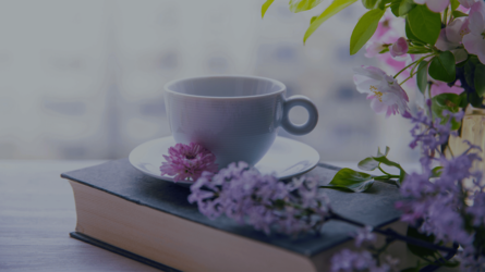 Eine weiße Tasse steht auf einem Buch, Blumen liegen davor