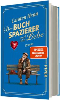 Das Buchcover zeigt vor blauem Hintergrund einen älteren Mann mit Mantel, Mütze und Stock auf einer Parkbank, neben ihm ein Stapel Bücher und eine rote Herzluftballon-Skizze. Titel in großer goldener Schrift: „Der Buchspazierer und die Liebe“, oben Autorname „Carsten Henn“, darunter klein „Roman“. Rechts ein rotes Rechteck mit weißer Aufschrift „SPIEGEL Bestseller-Autor“. Stimmung: nostalgisch, warm.