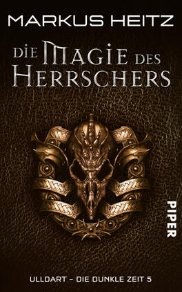 Das Buchcover zeigt eine dunkle, lederartige Textur im Hintergrund. Im Mittelpunkt befindet sich ein kunstvoll gestaltetes, goldenes Wappen mit einem Schädel und verzierten Elementen. Der Titel „Die Magie des Herrschers“ ist in eleganter, silberner Schrift platziert und hebt sich von der dunklen Oberfläche ab. Der Name des Autors, Markus Heitz, steht oben in klaren, weißen Buchstaben. Unten rechts ist das Verlagslogo „Piper“ in einer schlichten Schrift. Die Gesamtatmosphäre vermittelt ein Gefühl von Mystik und Abenteuer.