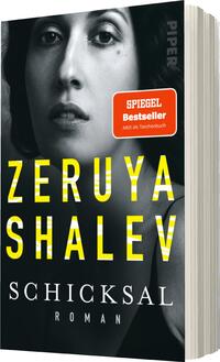 Das Buchcover zeigt ein Portrait einer Frau mit intensiven, nachdenklichen Gesichtszügen und dunklem Haar, das im Halbprofil dargestellt ist. Im Hintergrund dominieren schwarze Farbtöne, während der Titel „Zeruya Shalev“ in großen, gelben Buchstaben leuchtet. Darunter steht der Titel „Schicksal“ in subtilerer Schrift, gefolgt von dem Wort „Roman“. Ein rotes Label mit weißer Schrift informiert über den Status als „SPIEGEL Bestseller“ und die Verfügbarkeit als Taschenbuch. Die Atmosphäre ist geheimnisvoll und einladend zugleich.