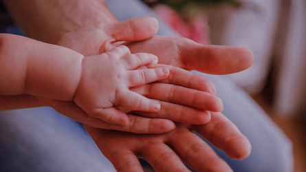 Eine Babyhand liegt auf zwei erwachsenen Händen