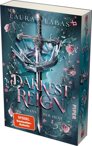 Das Buchcover zeigt eine dramatische Kombination aus einem silbernen, mit Dornen verzierten Schwert und einer Krone im Mittelpunkt, die in den Vordergrund ragt. Der Hintergrund ist in einem sanften Aquablau gestaltet, ergänzt durch filigrane, rosa Rosen und schimmernde Elemente, die eine mystische Atmosphäre erzeugen. Der Titel „DARKEST REIGN“ ist groß und prominent in eleganter, verschnörkelter Typografie in Weiß und Rosé gehalten. Darunter steht in kleinerer Schrift „im Bann der Hexe“. Am unteren Rand befindet sich ein orangefarbener Button mit dem Text „SPIEGEL-Bestseller-Autorin“.