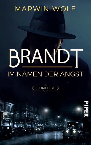 Das Buchcover zeigt einen geheimnisvollen Mann in einem Hut, dessen Gesicht im Schatten verborgen bleibt. Im Hintergrund sind unscharfe Silhouetten von Stadtgebäuden und Fahrzeugen in dunklen Farben zu sehen, was eine düstere Atmosphäre erzeugt. Der Titel „BRANDT“ ist in großen, modernen Buchstaben in Weiß und Gold gehalten, die den Blick auf sich ziehen. Darunter steht in kleineren Buchstaben „IM NAMEN DER ANGST“. Der Begriff „THRILLER“ ist in einem schmalen Banner platziert. Oben steht der Name des Autors „MARWIN WOLF“.