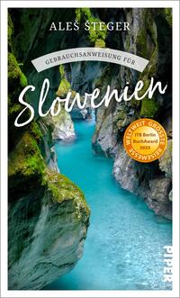 Das Buchcover zeigt eine beeindruckende Schlucht mit leuchtend blauem Wasser und grünem, felsigem Ufer. Der Titel „Gebrauchsanweisung für Slowenien“ ist in eleganter, hellweißer Schrift mittig platziert, während der Autorname Ales Šteger in kleinerer Schrift darunter steht. In der oberen Ecke befindet sich ein runder, orangefarbener Aufkleber mit dem Text „WELTWEIT GRÖSSTE REISESEMS“ sowie dem Hinweis „ITB Berlin BuchAward 2023“. Der Hintergrund strahlt eine ruhige, einladende Atmosphäre aus.
