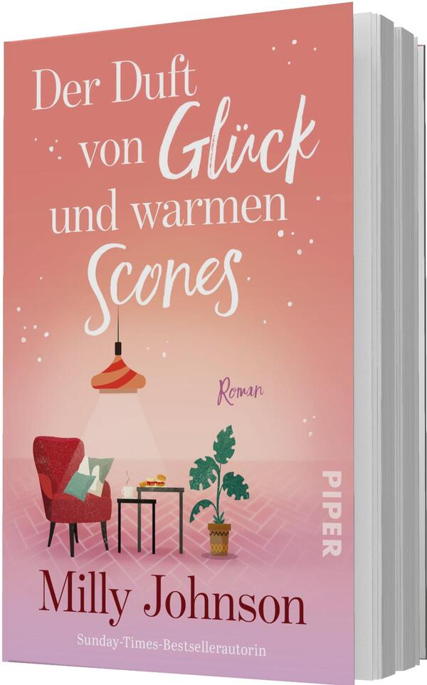Das Buchcover zeigt einen warmen Korall‑bis‑Rosé‑Verlauf als Hintergrund; groß der Titel „Der Duft von Glück und warmen Scones“ in weißer Kombination aus Serif‑ und handschriftlicher Script‑Typografie. Darunter die kleine Einordnung „Roman“ und unten der Autorenname Milly Johnson. Illustrierte Szene: ein roter Sessel mit grünem Kissen, ein kleiner Tisch mit Scones, eine hängende Lampe, eine Topfpflanze und dezente Lichtpunkte erzeugen eine gemütliche, einladende Atmosphäre.