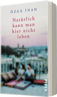 Das Buchcover zeigt eine sanfte, pastellfarbene Gestaltung in überwiegend blauen und pinken Tönen. Im Vordergrund sind zwei Personen auf einem gepolsterten Untergrund zu sehen, die entspannt miteinander interagieren. Der Titel „Natürlich kann man hier nicht leben“ ist in einer auffälligen roten Schrift mittig platziert, während der Autor Özgé İnan oben in blauer Schrift hervorgehoben ist. Die Hintergrundgestaltung vermittelt eine ruhige, nachdenkliche Atmosphäre. Das Wort „Roman“ befindet sich in kleinerer Schrift unter dem Titel.
