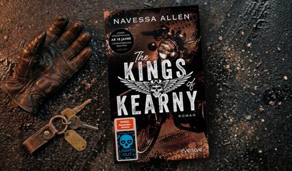 „The Kings of Kearny“ liegt auf dunklem Boden mit Reifenspuren. Links daneben liegen ein brauner Lederhandschuh und ein Schlüsselbund mit einem Anhänger.