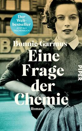 Das Buchcover zeigt eine schwarz-weiß gehaltene Fotografie einer Frau in einem eleganten grauen Kleid mit weißem Kragen. Sie hat lockige Haare und blickt direkt in die Kamera. Im Hintergrund ist ein unscharfer Schriftzug zu erkennen. Oberhalb der Frau steht in kräftigem Weiß der Titel „Eine Frage der Chemie“, gefolgt vom Zusatz „Roman“ in kleinerer Schrift. Darunter ist der Name der Autorin, Bonnie Garmus, platziert. Oben links befindet sich ein blauer Kreis mit dem Text „Der Bestseller“ und „Jetzt als Taschenbuch“.