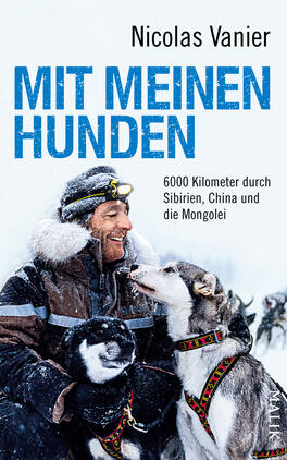 Das Buchcover zeigt einen grinsenden Mann mit dunklem Bart in einer winterlichen Landschaft, umgeben von mehreren Hunden. Die Tiere sind meist in Grau- und Schwarztönen gehalten, während der Mann eine warme, helle Jacke trägt. Der Titel „MIT MEINEN HUNDEN“ ist in großen, hellblauen Buchstaben prominent platziert, unter dem sich der Untertitel „6000 Kilometer durch Sibirien, China und die Mongolei“ in schlichter Schrift befindet. Der Autorname „Nicolas Vanier“ steht oben auf dem Cover in dezentem Schwarz.