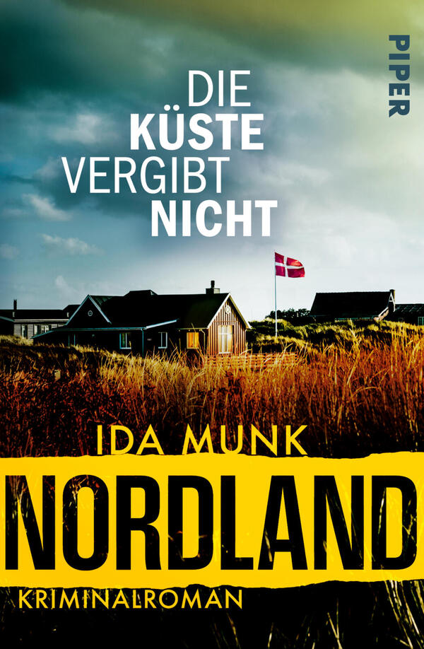 Das Buchcover zeigt eine düstere Küstenlandschaft mit stürmischem blau-grünem Himmel, vereinzelten niedrigen Häusern, einem Dänemark-Fähnchen auf einer Flagge und goldbraunen Strandgräsern im Vordergrund. Oben steht der Titel „Die Küste vergibt nicht“ in weißer Großschrift. Darunter erscheint der Autorenname „Ida Munk“ und ein breiter gelber Balken mit großem schwarzen Schriftzug „NORDLAND“ sowie dem kleinen Hinweis „Kriminalroman“. Atmosphäre: rau, spannungsgeladen.