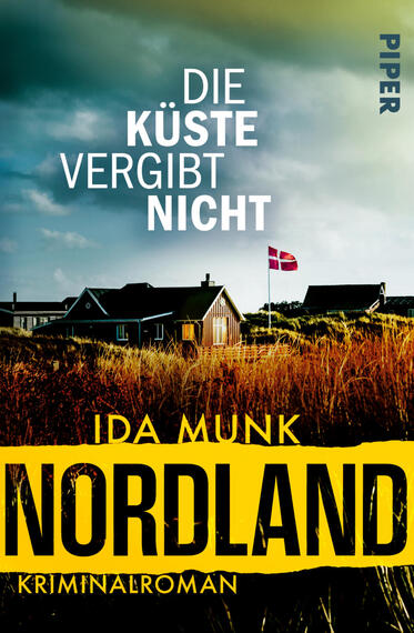 Das Buchcover zeigt eine stürmisch-dunkle Küstenlandschaft mit hohen, goldbraunen Strandgräsern im Vordergrund und dunklen Häusern auf einer Düne im Hintergrund; auf einer Fahnenstange weht eine rote dänische Flagge. Titel „Die Küste vergibt nicht“ in großen weißen Großbuchstaben oben, Autor „Ida Munk“ in gelb mittig, darunter auf schwarzem Grund der gelbe Banner mit großem schwarzen Schriftzug „NORDLAND“ und dem Zusatz „Kriminalroman“.