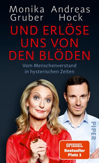 Das Buchcover zeigt zwei Personen in der Mitte: eine Frau mit blonden, lockigen Haaren und einem rot-blauen Outfit sowie einen Mann mit kurzen, dunklen Haaren in einem hellen Hemd. Der Hintergrund ist dunkelblau und vermittelt eine ernsthafte Atmosphäre. Der Titel „UND ERLÖSE UNS VON DEN BLÖDEN“ ist in großen roten Buchstaben geschrieben, darüber stehen die Autoren „Monika Gruber“ und „Andreas Hock“ in Weiß. Am unteren Rand befindet sich der Vermerk „SPIEGEL Bestseller Platz 1“ und das Verlagslogo „PIPER“.