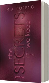 Das Buchcover zeigt einen eleganten, farbverlaufartigen Hintergrund in verschiedenen Lila- und Rottönen. Im Zentrum steht der Titel „the SECRETS we keep“ in großen, geschwungenen Buchstaben, die einen modernen Schriftstil verkörpern. Die Schrift wirkt glänzend und dynamisch. Der Name der Autorin, „Mia Moreno“, befindet sich oben und ist in einer schlichten Schriftart gehalten. Am unteren Rand ist das Wort „Roman“ in einer handschriftlichen, verschnörkelten Schrift präsentiert.