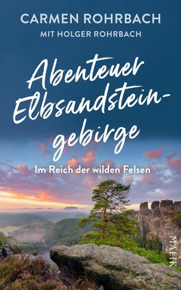 Abenteuer Elbsandsteingebirge – Im Reich der wilden Felsen Das Buchcover zeigt eine beeindruckende Landschaft des Elbsandsteingebirges mit einer dramatischen Bergkulisse im Hintergrund. Die Farben sind dominiert von sanften Blau- und Violetttönen, die bei Sonnenaufgang eine ruhige Atmosphäre erzeugen. In der oberen Hälfte steht der Titel „Abenteuer Elbsandsteingebirge“ in dynamischer, handschriftlicher Schrift, während der Untertitel „Im Reich der wilden Felsen“ in klarer, lesbarer Schrift darunter platziert ist. Die Autoren Carmen Rohrbach und Holger Rohrbach sind am oberen Rand in einer eleganten Schriftart aufgeführt.