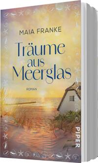 Das Buchcover zeigt eine friedliche Küstenszene mit einem sanften Farbverlauf in warmen Gelb- und Orangetönen, die an einen Sonnenuntergang erinnern. Im Vordergrund ist ein Sandstrand mit Gräsern, während im Hintergrund ein weißes Haus steht, das teilweise verdeckt von der Vegetation ist. Über dieser idyllischen Landschaft prangt der Titel „Träume aus Meerglas“ in eleganter, geschwungener Schrift, gefolgt von dem Namen der Autorin Maia Franke. Die Atmosphäre vermittelt ein Gefühl von Ruhe und Sehnsucht.
