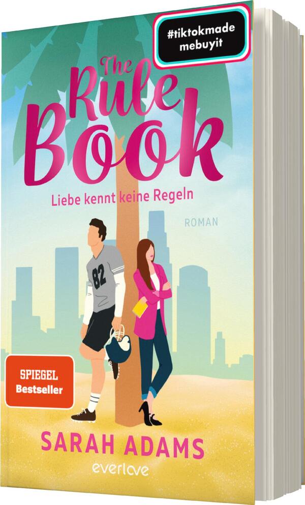 Das Buchcover zeigt einen sonnigen Strand mit Palmen, in sanften Pastellfarben. Im Vordergrund stehen zwei Figuren: ein Mann in sportlicher Kleidung mit der Nummer 82 und eine Frau in einem pinken Kleid, die zusammen lachen. Über dem Bild ist der Titel „The Rule Book“ in großen, auffälligen Buchstaben zu sehen, gefolgt von „Liebe kennt keine Regeln“ in kleinerer Schrift. Unten steht der Name der Autorin „SARAH ADAMS“ und das Wort „ROMAN“. In der oberen Ecke befindet sich ein Hashtag.