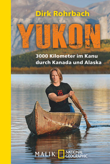 Das Buchcover zeigt einen Mann in einem Kanu, der auf einem ruhigen Gewässer paddelt, umgeben von majestätischen Bergen. Die Farben sind vorwiegend in sanften Naturtönen gehalten, während der Titel „YUKON“ in großen, orangen Buchstaben hervorsticht. Darunter steht der Untertitel „3000 Kilometer im Kanu durch Kanada und Alaska“ in kleinerer Schrift. Der Autor, Dirk Rohrbach, ist am oberen Rand des Covers in schlichter, schwarzer Schrift zu sehen. Die Gesamtatmosphäre vermittelt Abenteuer und Naturverbundenheit.