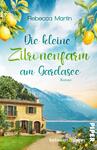 Das Buchcover zeigt eine malerische Landschaft am Gardasee mit einem charmanten, zweistöckigen Haus in warmen Erdtönen. Im Vordergrund sprießen grüne Pflanzen und Zitronen hängen fruchtig von den Bäumen. Der Himmel ist blau mit sanften Wolken, im Hintergrund erheben sich die Berge. In geschwungener, grüner Schrift steht der Titel „Die kleine Zitronenfarm am Gardasee“ von Rebecca Martin. Darunter befindet sich der Hinweis „Roman“ in schlichter Schrift. Die Atmosphäre vermittelt Idylle und mediterranes Flair.