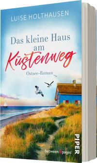 Das Buchcover zeigt eine idyllische Ostsee-Landschaft mit einem kleinen blauen Haus am Küstenweg. Der Himmel ist hellblau mit sanften Wolken, während die Wellen sanft an den Strand schlagen. Im Vordergrund sind grüne Gräser und Sanddünen zu sehen. Der Titel „Das kleine Haus am Küstenweg“ ist in auffälligen roten Buchstaben gestaltet, während die Schriftart für „Ostsee-Roman“ klein und dezent gehalten ist. Der Name der Autorin, Luise Holthausen, steht oberhalb des Titels in Weiß.