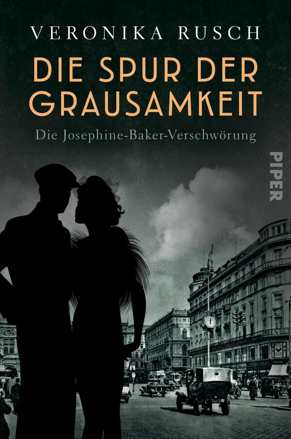 Das Buchcover zeigt eine düstere, historische Straßenszene mit einem Pärchen im Vordergrund, das sich umarmt. Die Silhouetten der Figuren sind in Schwarz gehalten, während der Hintergrund in grauen und blauen Tönen gestaltet ist. Der Titel „DIE SPUR DER GRAUSAMKEIT“ erscheint in auffälligem Orange und ist gut lesbar. Darunter steht „Die Josephine-Baker-Verschwörung“ in einer schlichteren Schriftart. Der Name der Autorin, Veronika Rusch, befindet sich am oberen Rand in Weiß. Die gesamte Atmosphäre ist geheimnisvoll und ansprechend.