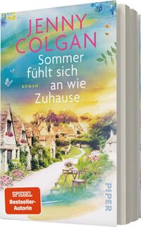 Das Buchcover zeigt eine idyllische Landschaft mit charmanten, ländlichen Häusern und bunten Blumen auf einem Weg, der zu einem warmen, einladenden Himmel führt. Der Titel „Sommer fühlt sich an wie Zuhause“ ist in einer verspielten, hellen Schriftart in Weiß und Pink gehalten, während der Autorennamen „JENNY COLGAN“ prominent oben in Pink erscheint. Die Atmosphäre strahlt Wärme und Geborgenheit aus. Am unteren Rand befindet sich ein rotes Feld mit der Aufschrift „SPIEGEL Bestseller-Autorin“.