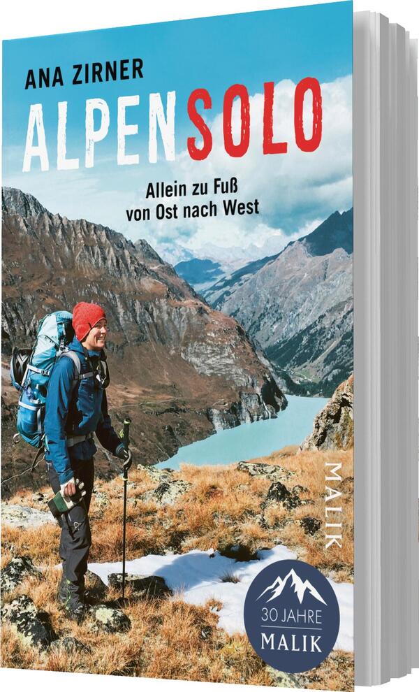 Das Buchcover zeigt einen Wanderer in alpiner Landschaft, gekleidet in eine blaue Jacke und mit roter Mütze, der einen Rucksack trägt und auf einem gebirgigen Terrain steht. Im Hintergrund sind majestätische Berge und ein türkisfarbener See sichtbar. Der Titel „ALPENSOLO“ erscheint in großen, rot und blau kontrastierenden Buchstaben. Darunter steht der Untertitel „Allein zu Fuß von Ost nach West“ in schlichter Schrift. Das Verlagslogo „30 Jahre Malik“ befindet sich im unteren Bereich des Covers.