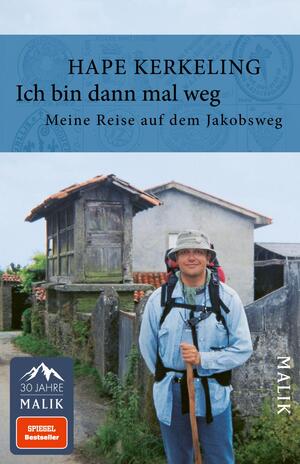 Das Buchcover zeigt einen lächelnden Hape Kerkeling, der mit einem Rucksack und Wanderausrüstung auf einem Weg steht. Im Hintergrund sind traditionelle Gebäude und grüne Landschaften zu sehen. Der obere Teil des Covers ist in einem hellen Blau gehalten, darüber steht der Titel „Ich bin dann mal weg“ in großer, schwarzer Schrift. Darunter steht der Untertitel „Meine Reise auf dem Jakobsweg“ in kleinerer Schrift. In der unteren linken Ecke befindet sich das Logo „30 Jahre Malik“.