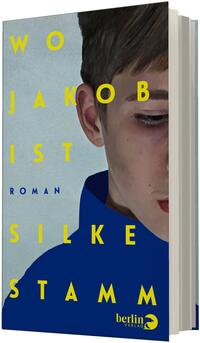 Das Buchcover zeigt auf hellgrauem Grund die realistische Porträtansicht eines Jungen mit kurzem braunem Haar, nur rechte Gesichtshälfte sichtbar, in einem blauen Kapuzenpullover; gelbe Großbuchstaben bilden den Titel „WO JAKOB IST“ über das Bild verteilt, der Autorenname „SILKE STAMM“ steht ebenfalls in Gelb, links unten klein der Hinweis „ROMAN“ in Blau. Stimmung ruhig, nachdenklich.