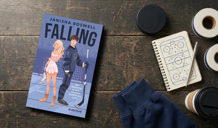 „Falling“ liegt auf einem Holztisch. Rechts daneben liegen ein schwarzer Puck, ein Notizbuch und ein Kaffeebecher und die Ärmel eines dunkelblauen Hoodies sind zu sehen.