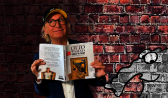  Otto Waalkes steht mit seinem Buch „Kunst in Sicht“ in der Hand vor einer Backsteinmauer mit aufgemaltem Ottifant