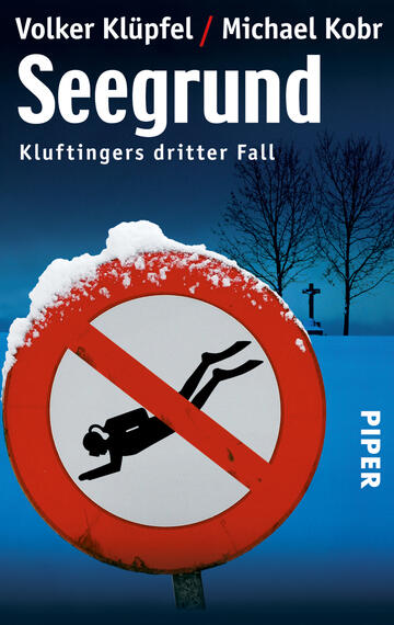 Das Buchcover zeigt eine winterliche Landschaft mit einem schneebedeckten Boden und kahlen Bäumen im Hintergrund. Im Vordergrund ist ein rotes Verkehrsschild mit einer schwarzen Figur, die ins Wasser fällt, zu sehen, umrahmt von einer weißen Schneekante. Der Titel „Seeggrund“ in großer, weißer Schrift oben gehört zu den Autoren Volker Klüpfel und Michael Kobr, deren Namen in kleinerer Schrift darunter stehen. Am rechten Rand ist das Verlagslogo „PIPER“ abgedruckt.