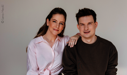 Jennifer Sieglar und Tim Schreder sitzen nebeneinander, in rosa Hemd und braunem Sweatshirt.