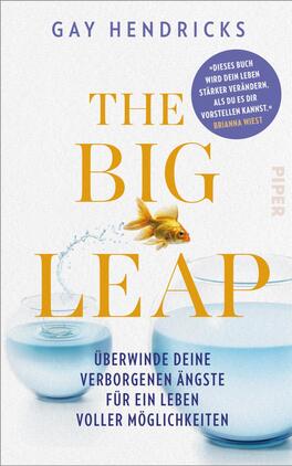 Das Buchcover zeigt einen minimalistischen und farbenfrohen Entwurf. In der oberen Hälfte steht der Autorenname „GAY HENDRICKS“ in schwarzer Schrift. Der Titel „THE BIG LEAP“ ist in großer, gelber Schrift mittig platziert. Darunter befindet sich der Untertitel „Überwinde deine verborgenen Ängste für ein Leben voller Möglichkeiten“ in kleinerer Schrift. Ein goldiger Fisch springt aus einem runden Glasbehälter, der mit klarem Wasser gefüllt ist. In der oberen rechten Ecke ist ein blauer Button mit dem Text „„Dieses Buch wird dein Leben stärker verändern, als du es dir vorstellen kannst““ abgebildet.