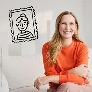 Franca Cerutti sitzt auf einer beigen Couch. Links neben ihr ist ein einfach illustriertes Porträt einer älteren Frau in einem Rahmen abgebildet.