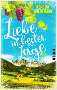 Das Buchcover zeigt eine idyllische Landschaft mit sanften Hügeln und imposanten Bergen im Hintergrund. Oben sind grüne Weinblätter und lila Trauben platziert. Der Himmel ist in einem leuchtenden Blau gehalten. Der Titel „Liebe in bester Lage“ ist in geschwungener, weißer Schrift zentral platziert, darunter der Hinweis „Roman“ in kleinerer Schrift. Der Name der Autorin, Kerstin Wiedemann, steht in gelber Schrift oben links, während das Verlagslogo „PIPER“ am rechten Rand zu finden ist.
