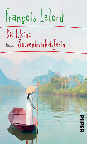 Das Buchcover zeigt eine ruhige Landschaft mit einem schmalen, roten Boot, in dem eine junge Frau mit einem weißen Hut sitzt und ein Paddel hält. Im Hintergrund sind sanfte, grüne Hügel und ein spiegelglattes Wasser zu sehen, das die Umgebung reflektiert. Der Titel „Die kleine Souvenirverkäuferin“ und der Autor François Lelord sind in verspielter, handschriftlicher Typografie in kräftigen Farben über dem Bild platziert. Die Atmosphäre vermittelt Ruhe und einen Hauch von Abenteuer.