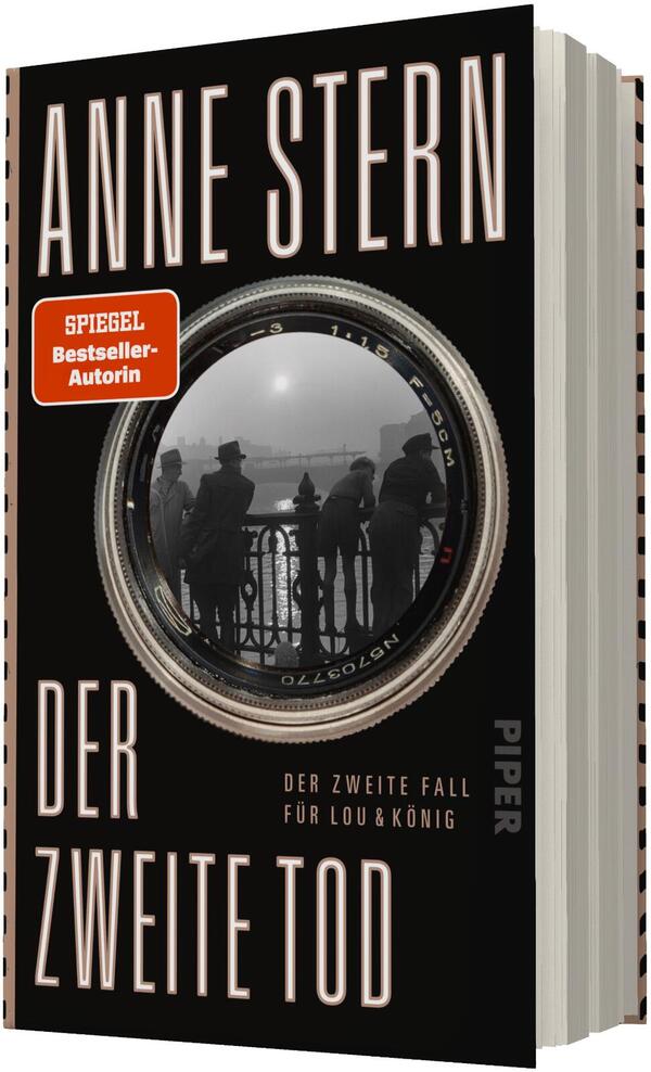 Das Buchcover zeigt einen schwarzen Hintergrund mit großflächiger, hochgezogener beiger Typografie für den Autorennamen „ANNE STERN“ und den Titel „DER ZWEITE TOD“. Zentral ist eine große Kameralinse, in deren Glas eine schwarzweiß-Fotoaufnahme von silhouettierten Personen an einem Brückengeländer sichtbar ist. Ein oranger, aufgeklebter Button links oben trägt den Text „SPIEGEL Bestseller-Autorin“. Der Eindruck ist düster, geheimnisvoll und noir-haft.