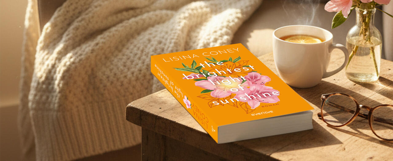 „The Brightest Light of Sunshine“ liegt auf einem Holztisch. Daneben stehen eine Tasse Tee mit Zitrone, eine Brille und eine Vase mit rosa Blumen. Im Hintergrund ist eine beige Decke sichtbar.