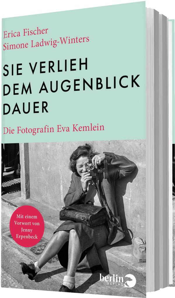 Das Buchcover zeigt oben einen hellmintgrünen Bereich mit den Autorennamen Erica Fischer und Simone Ladwig‑Winters in kleiner roter Schrift, darunter der Titel „SIE VERLIEH DEM AUGENBLICK DAUER“ in großer schwarzer Grotesk‑Versaltypografie und die rote Unterzeile „Die Fotografin Eva Kemlein“. Unten ein kontrastreiches schwarzweißes Foto: eine sitzende Frau mit Umhängetasche fotografiert mit einer Kamera, nüchterne, dokumentarische Stimmung.