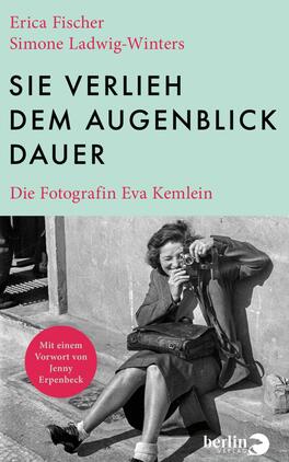 Das Buchcover zeigt im oberen Drittel ein mintgrünes Feld mit dem großen, schwarzen, serifenlosen Titel in Versalien „SIE VERLIEH DEM AUGENBLICK DAUER“; links oben stehen in roter Serifenschrift die Autorennamen Erica Fischer und Simone Ladwig-Winters, darunter in kleiner roter Serifenschrift der Untertitel Die Fotografin Eva Kemlein. Die untere Hälfte zeigt ein schwarzweißes Foto einer lächelnden Frau, die mit einer Kamera auf dem Gehsteig sitzt; Atmosphäre: nostalgisch, dokumentarisch.