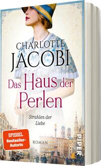 Das Buchcover zeigt eine elegante Frau mit einem modischen Hut und einer blauen Bluse, die den Betrachter direkt anschaut. Der Hintergrund zeigt eine historische Stadtansicht mit charakteristischen Gebäuden. Oben steht in größerer Schrift „CHARLOTTE JACOBI“, gefolgt von dem Titel „Das Haus der Perlen“ in großer, pinker Schrift. Darunter steht der Untertitel „Strahlen der Liebe“ in kleinerer Schrift. Das Cover vermittelt eine romantische und nostalgische Atmosphäre. Ein orangefarbenes Siegel mit der Aufschrift „SPIEGEL-Bestseller-Autorin“ hebt sich deutlich ab.