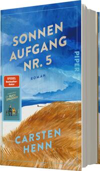 Das Buchcover zeigt einen weiten, hellblauen Himmel mit sanften, weißen Wolken und einem Horizont, der auf das Meer blickt. Im Vordergrund erstrecken sich goldene, weiche Grasstrukturen. Oben steht in großem, klaren Weiß „SONNEN AUFGANG NR. 5“, darunter in kleinerer Schrift „ROMAN“. Am linken oberen Rand ist ein rotes Badge mit der Aufschrift „SPIEGEL Bestseller-Autor“ zu sehen. Der Name des Autors, „Carsten Henn“, erscheint in dezentem Blau am unteren Rand.