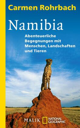 Das Buchcover zeigt einen Geparden, der majestätisch auf einem Felsen steht, mit einem weiten, blauen Himmel im Hintergrund. Der Titel „Namibia“ ist in großen, weißen Buchstaben in der Mitte des Covers platziert, während darunter der Untertitel „Abenteuerliche Begegnungen mit Menschen, Landschaften und Tieren“ in kleinerer Schrift dargestellt ist. Oben links steht der Name der Autorin, Carmen Rohrbach. Der Hintergrund ist in sanften Blautönen gehalten, was eine weite und offene Atmosphäre vermittelt.