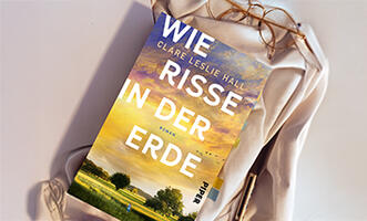 Buch mit dem Titel 'Wie Risse in der Erde' liegt auf einer weißen Stoff