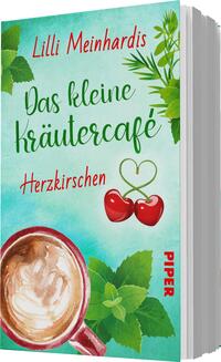 Das Buchcover zeigt einen hellen, mintgrünen Hintergrund, der mit stilisierten Blättern und Kräutern verziert ist. Oben steht in geschwungener, roter Schrift der Titel „Das kleine kräutercafé“ und darunter in etwas kleinerer Schrift das Wort „Herzkirschen“. In der unteren linken Ecke ist eine Tasse mit cremigem Kaffee und Milchschaum abgebildet. Das Design strahlt eine gemütliche, einladende Atmosphäre aus. Der Name der Autorin, Lilli Meinhardis, steht prominent oben. Am rechten Rand ist das Verlagslogo „PIPER“ in roter Schrift zu sehen.