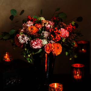 Blumenstrauß mit verschiedenen orangefarbenen Blumen. Daneben orangefarbene Teelichter.