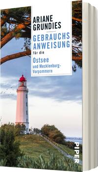 Das Buchcover zeigt einen weißen, stilisierten Leuchtturm, der vor einem klaren blauen Himmel und sanften Wolken steht. Im Vordergrund sind grüne Bäume zu sehen, die dem Cover eine natürliche Atmosphäre verleihen. Der Titel „Gebrauchsanweisung für die Ostsee und Mecklenburg-Vorpommern“ ist in blauer, moderner Schrift gestaltet, während der Autorennamen „Ariane Grundies“ in schwarzer Schrift darüber steht. Das Cover vermittelt ein Gefühl von Erholung und Naturverbundenheit.