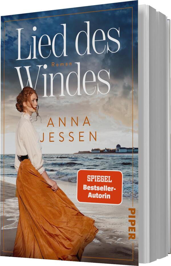 Das Buchcover zeigt eine Frau mit lockigem, rotem Haar, die in einem langen, orangefarbenen Rock am Strand steht. Der Hintergrund zeigt eine stürmische See unter einem bewölkten Himmel. Der Titel „Lied des Windes“ steht in großen, weißen Buchstaben oben, ergänzt durch das Wort „Roman“. Unter dem Titel befindet sich der Name „ANNA JESSEN“ in einer klaren Schrift. Ein rotes Label mit dem Text „SPIEGEL Bestseller-Autorin“ befindet sich in der unteren rechten Ecke.