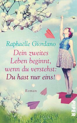 Das Buchcover zeigt eine fröhliche Frau in einem blauen Top und einem gemusterten Rock, die mit einer Hand gen Himmel zeigt. Um sie herum schweben bunte Papierflieger und sanfte weiße Blüten, die eine heitere, luftige Atmosphäre schaffen. Im oberen Drittel steht der Titel „Dein zweites Leben beginnt, wenn du verstehst: Du hast nur eins!“ in eleganter roter Typografie, während der Name der Autorin, Raphaëlle Giordano, in kleinerer Schrift darüber positioniert ist. Die Farbpalette ist freundlich und hell, dominierend sind Blau- und Pastelltöne.